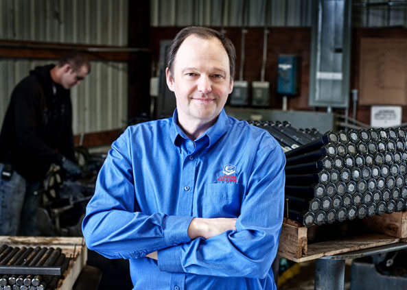 An image of a happy employee from Cascade Nut & Bolt in a blue dress shirt with his arms crossed